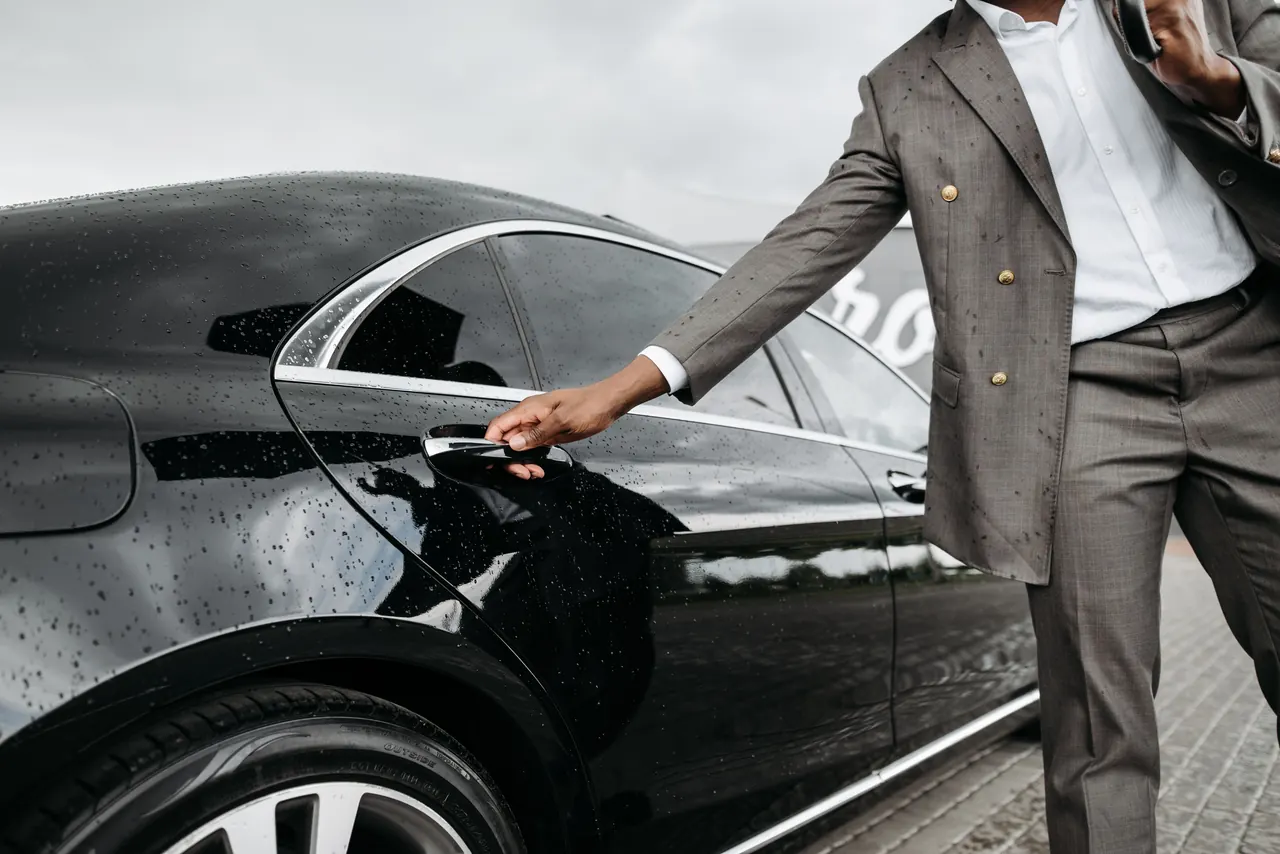 An AFSAHI chauffeur opening the door of a black Mercedes S-Class for an arriving passenger
