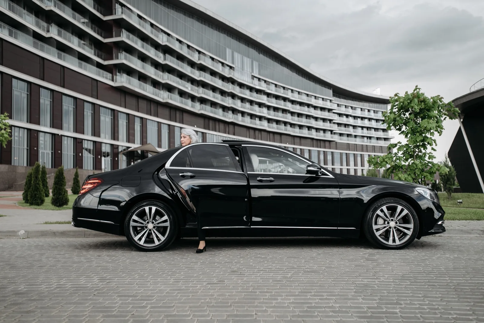 Black Mercedes-Benz S-Class with the rear door open in front of a modern hotel